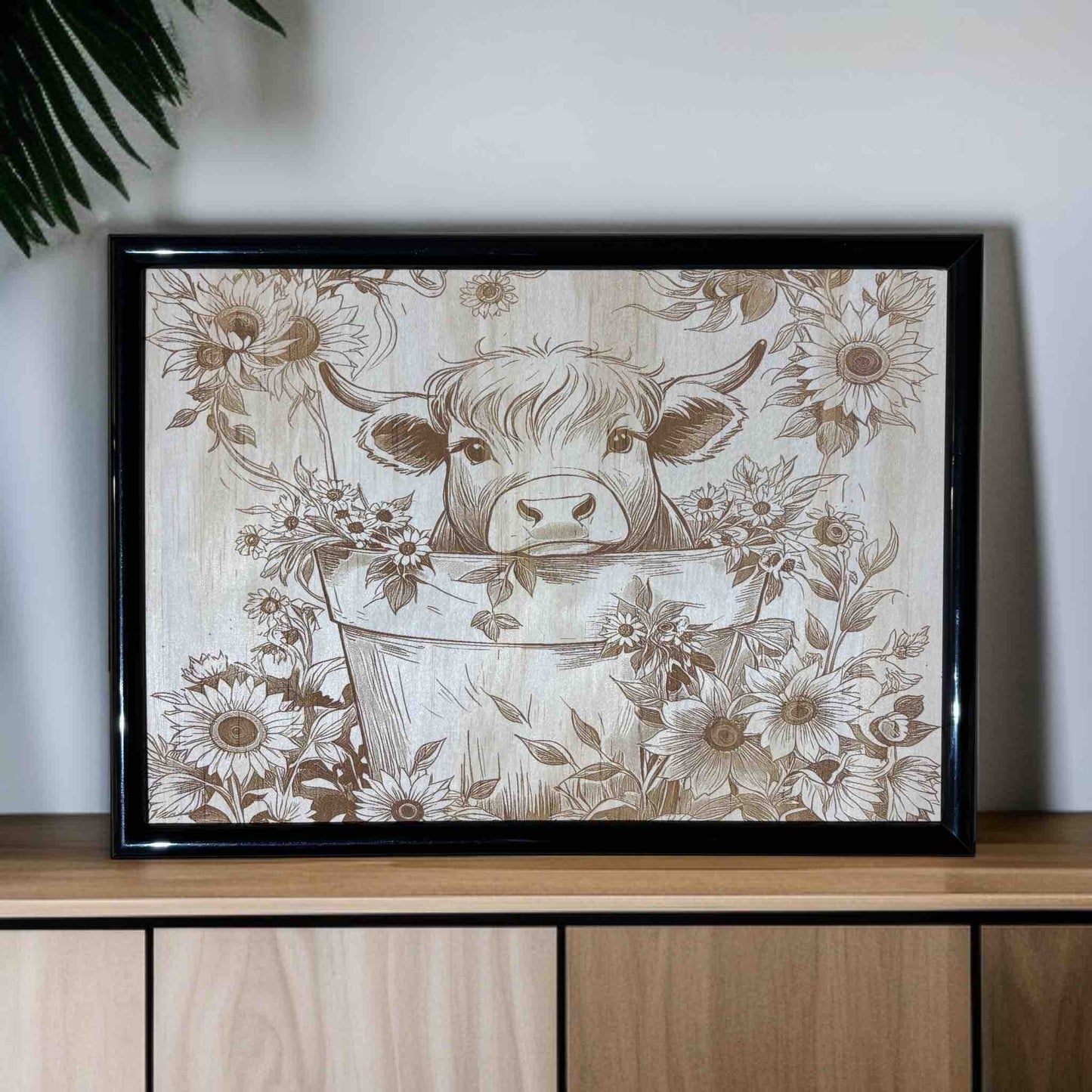 Framed artwork of a cow in a bucket with floral patterns on a wooden surface.