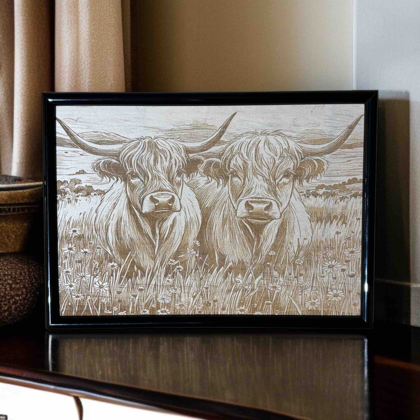 Framed artwork of two highland cows in a field on a wooden surface.
