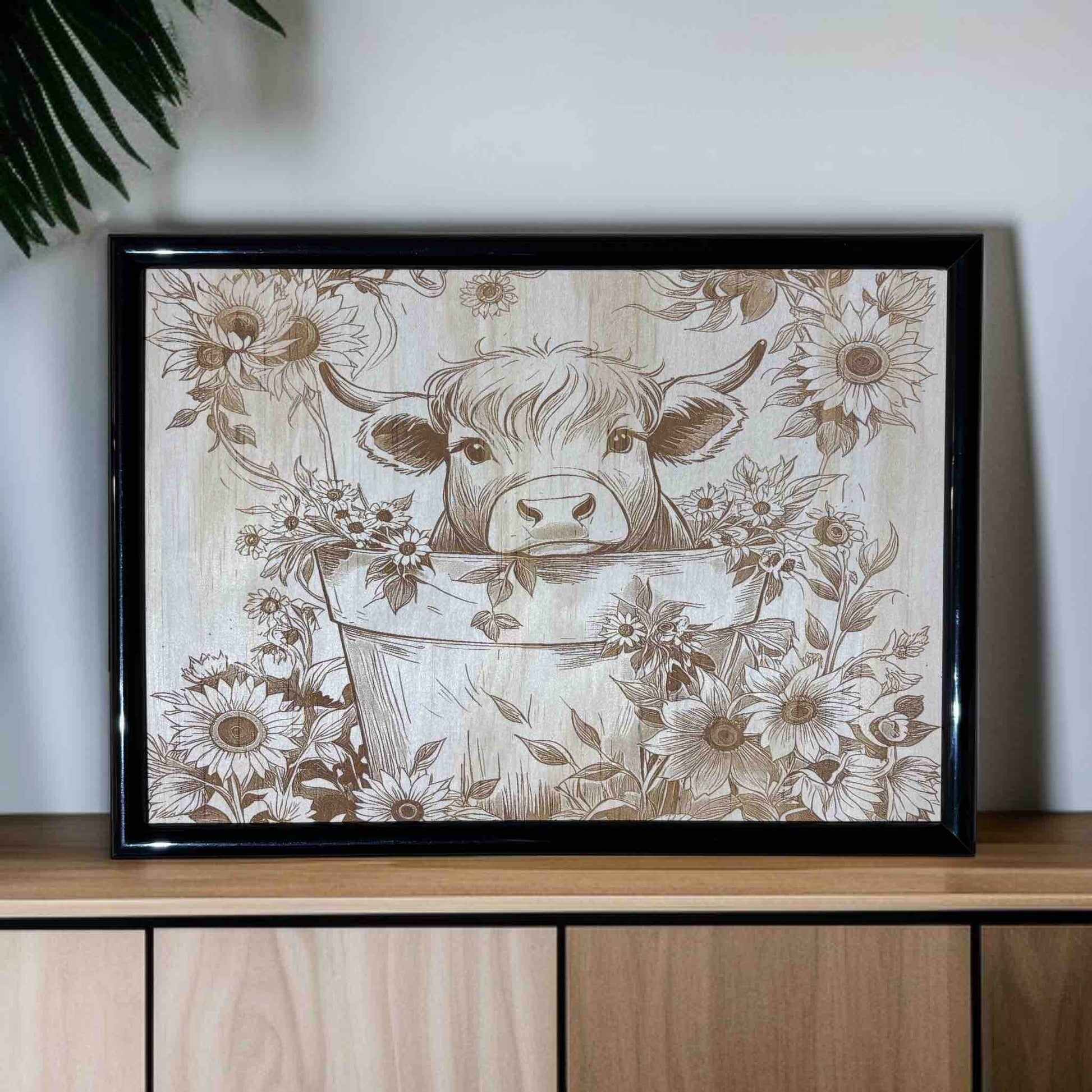 Framed artwork of a cow in a bucket with floral patterns on a wooden surface.