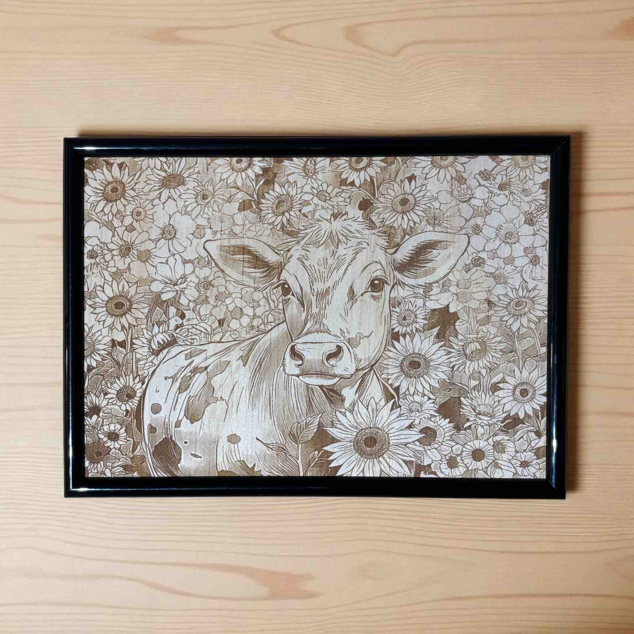 Framed artwork of a cow surrounded by floral patterns on a wooden surface