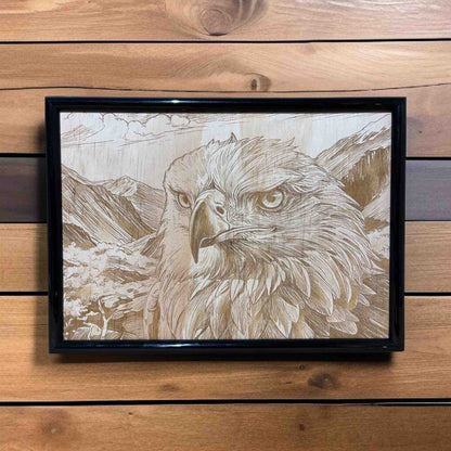 Framed artwork of an eagle with a mountainous background on a wooden wall.