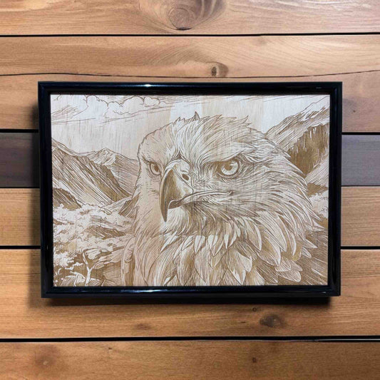 Framed artwork of an eagle with a mountainous background on a wooden wall.