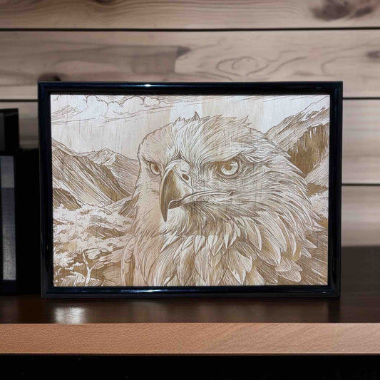 Framed artwork of an eagle with a mountainous background on a wooden surface.