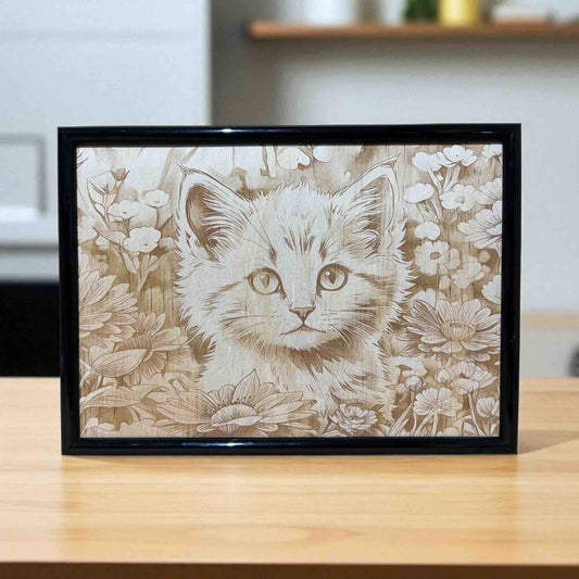 Framed artwork of a kitten surrounded by flowers on a wooden surface.
