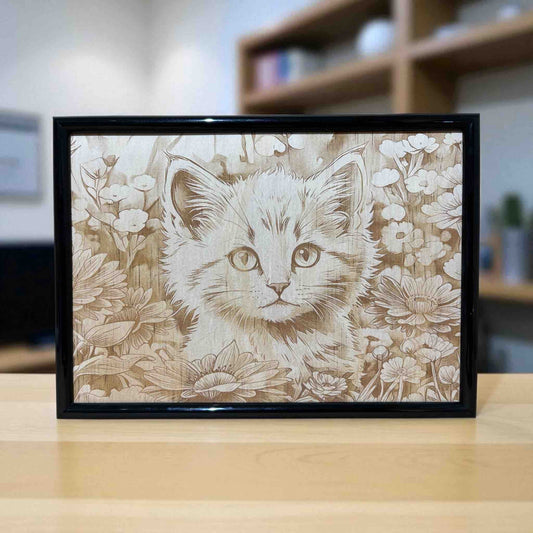 Framed artwork of a kitten surrounded by flowers on a wooden surface.