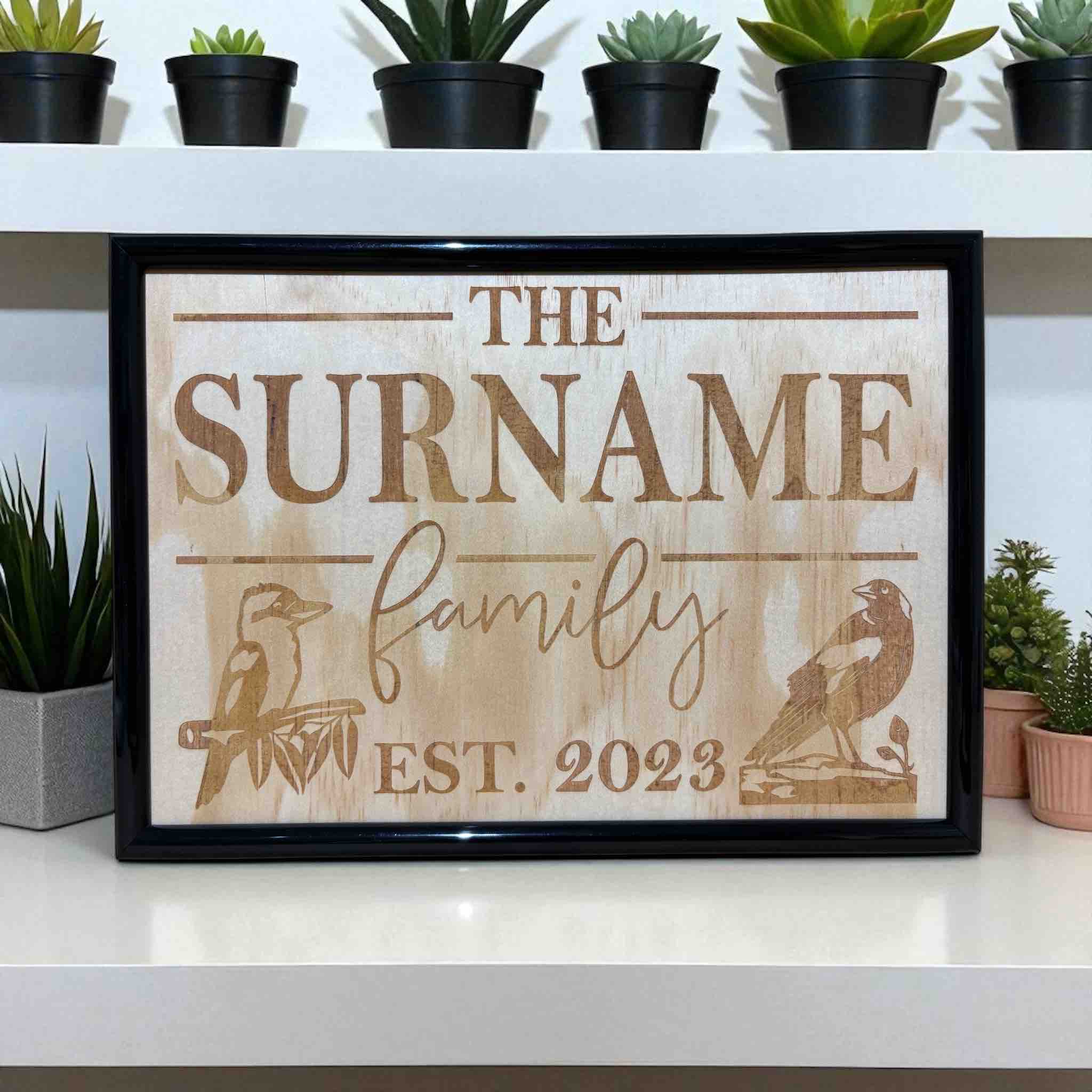 A personalised wood engraved framed design featuring the text 'The Surname family' with a Kookaburra and Magpie birds, Australian Made. Laser Design Creations