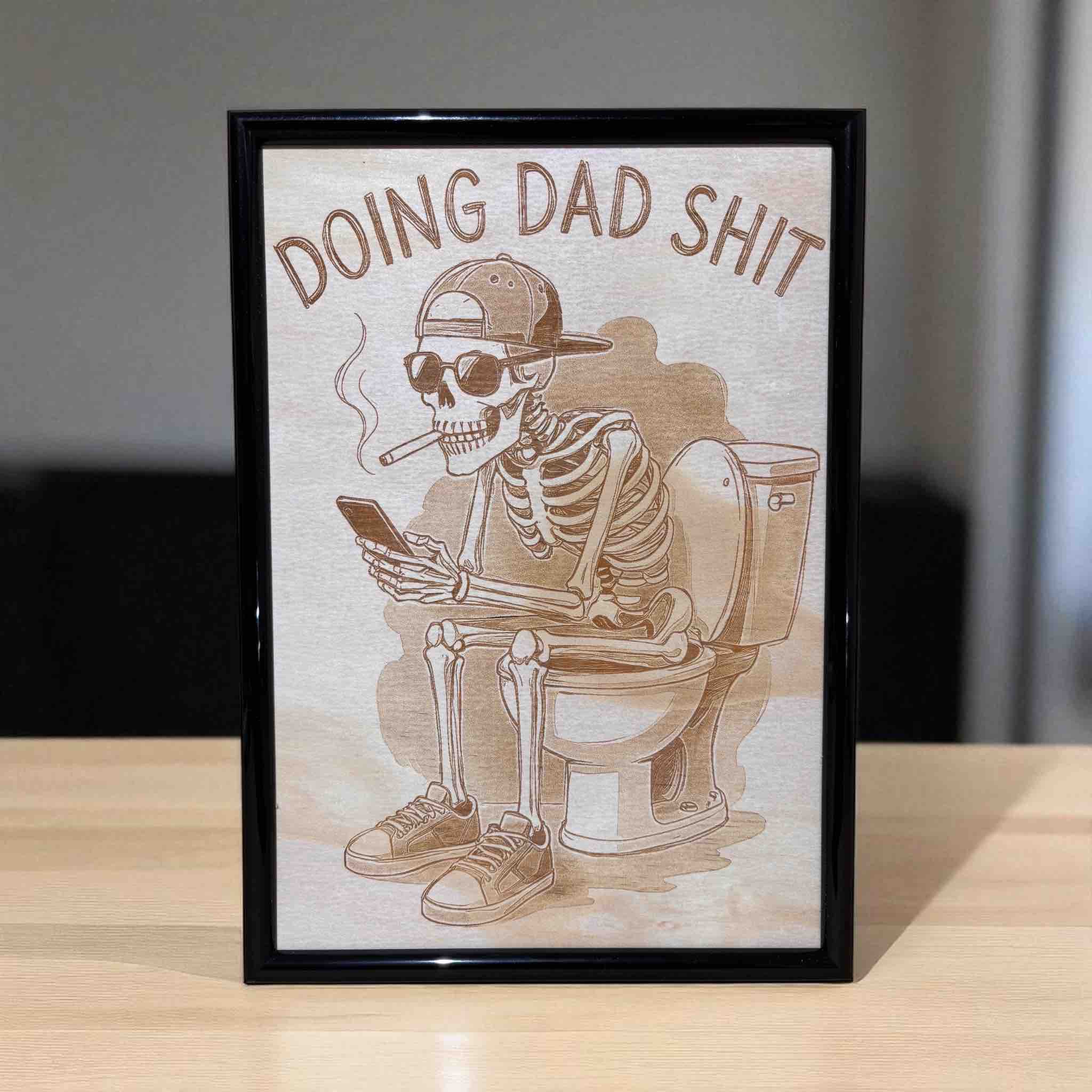 Framed wood engraved art featuring a skeleton dad sitting on a toilet, Laser Design Creations.