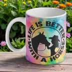 "Life is Better with a Horse" ceramic mug, featuring a silhouette of a cowgirl and her horse against a vibrant watercolour background.
