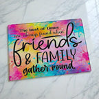Vibrant rainbow watercolour glass chopping board from Laser Design Creations featuring the heartwarming quote about friends and family gathering round, set against a colourful wash background.