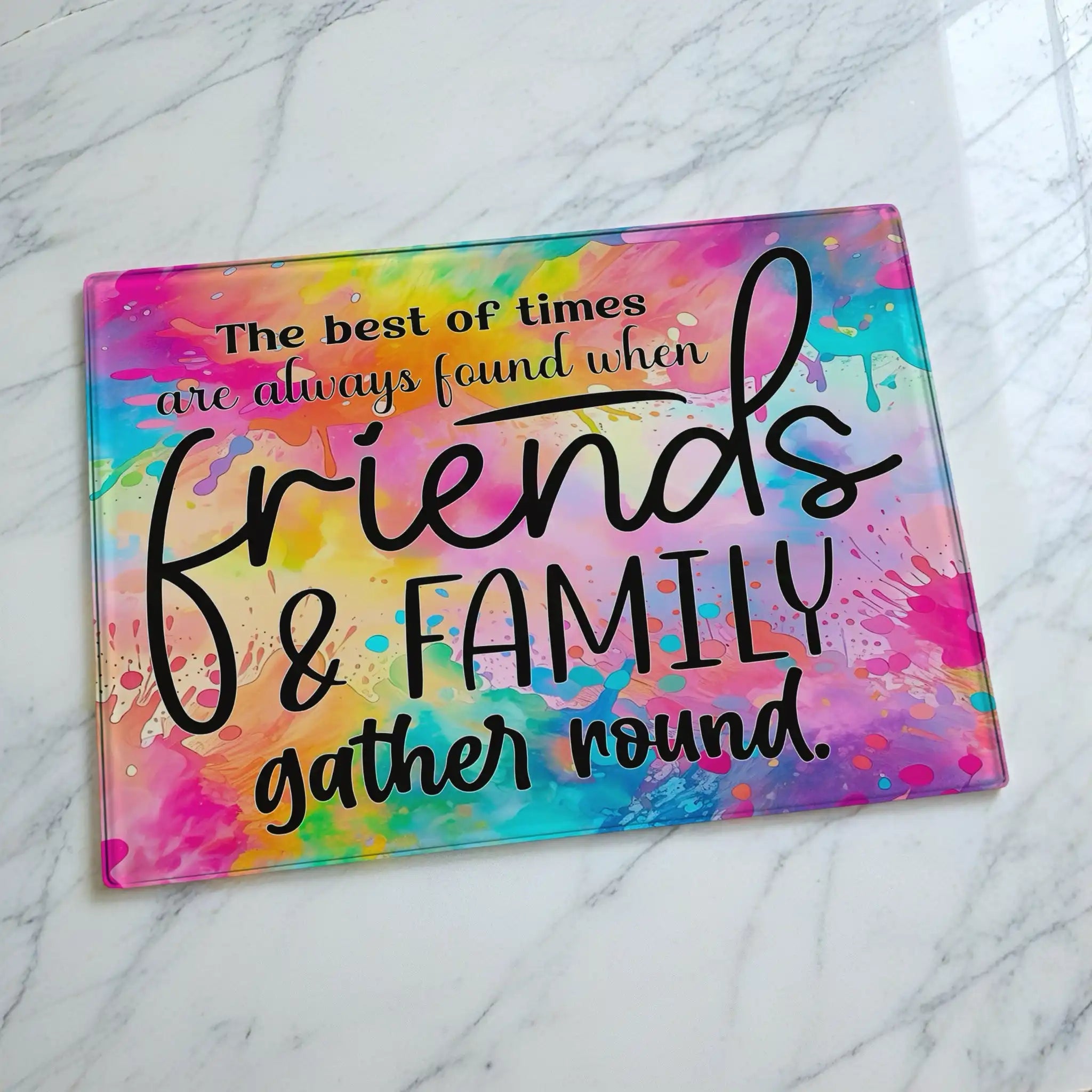 Vibrant rainbow watercolour glass chopping board from Laser Design Creations featuring the heartwarming quote about friends and family gathering round, set against a colourful wash background.