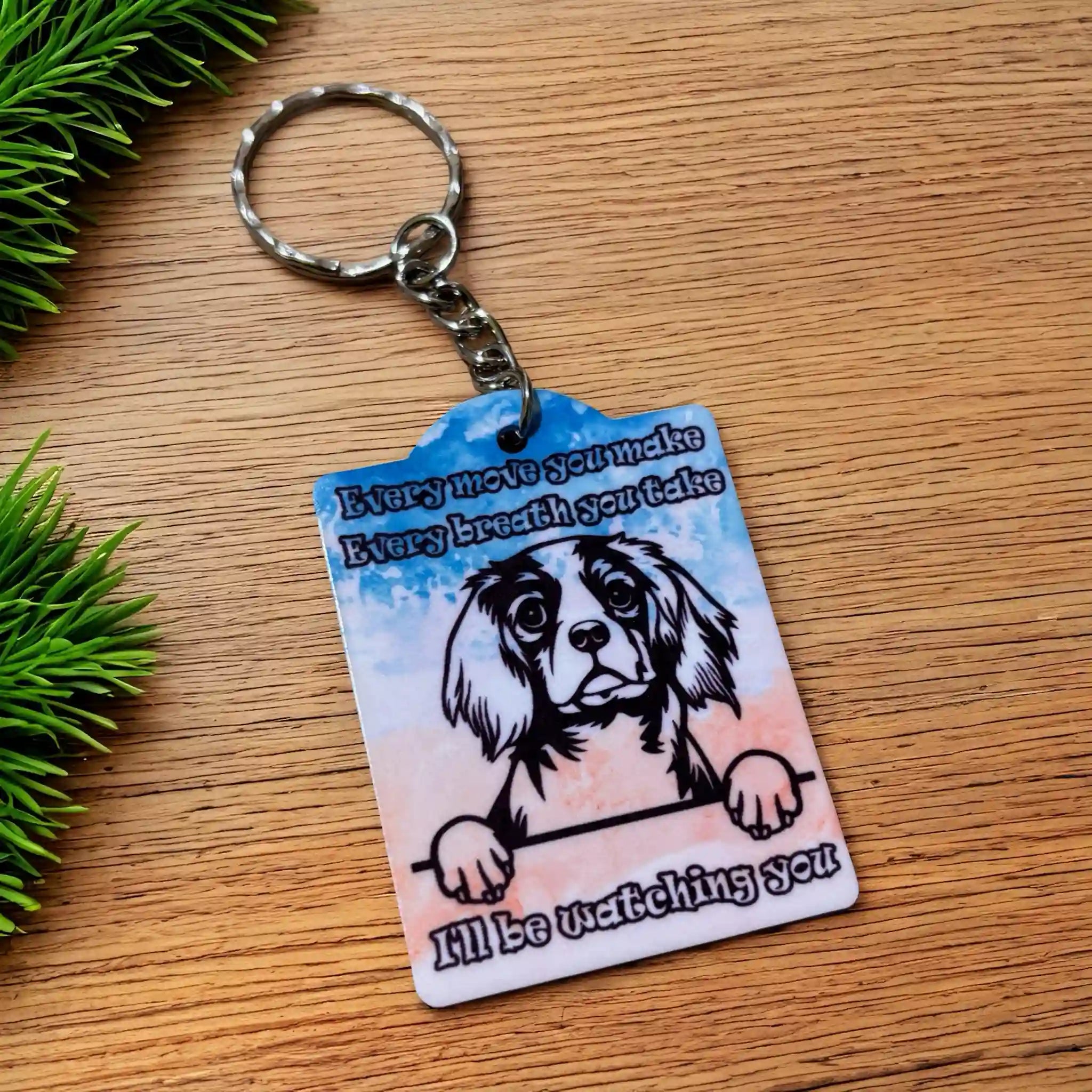 Side view of Every Move You Make Cavalier keyring, showcasing a humorous watercolour illustration of a Cavalier King Charles Spaniel dog with the text Every move you make Every breath you take I'll be watching you on a neutral background by Laser Design Creations.
