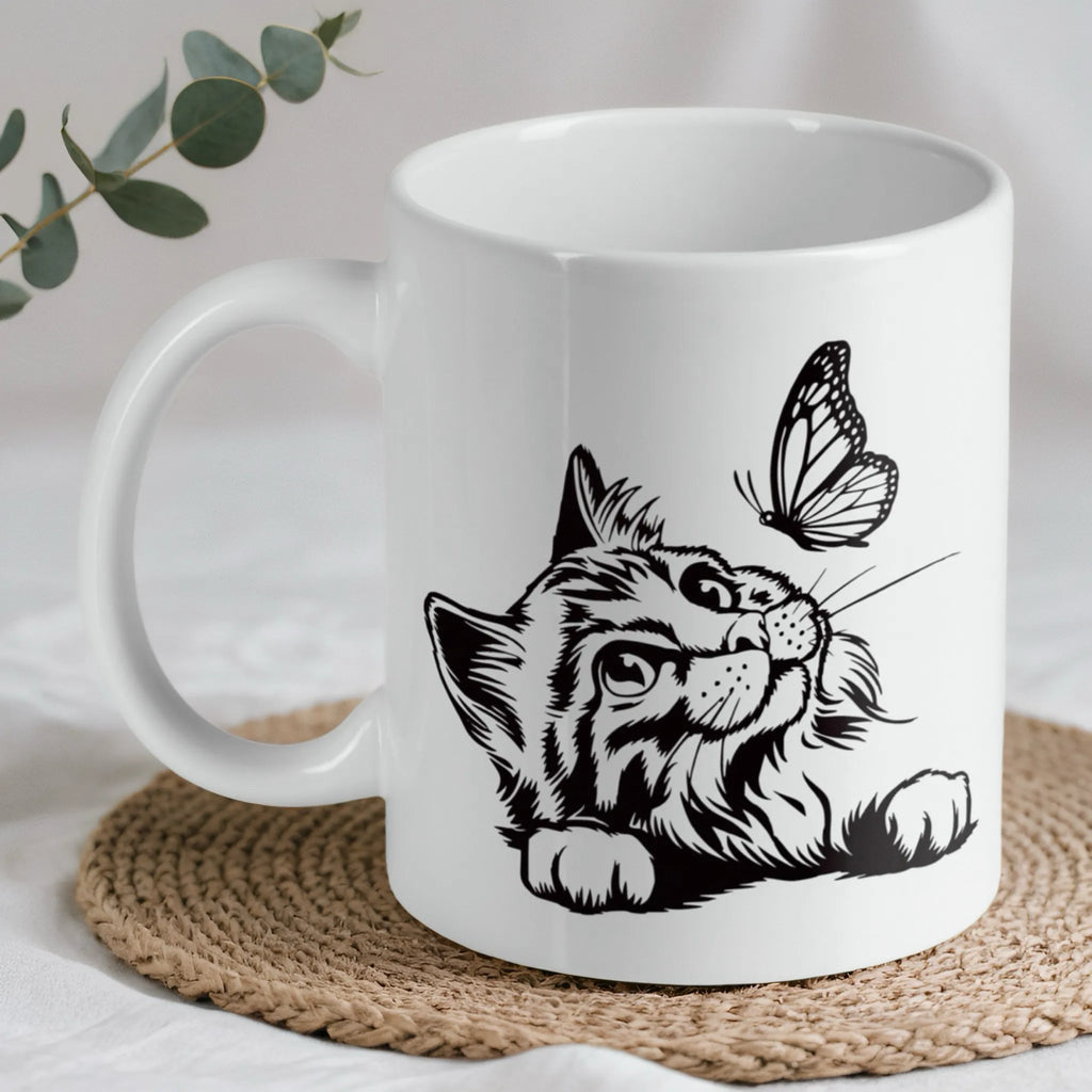Cat and butterfly line art ceramic mug by Laser Design Creations, featuring a black line art illustration of a fluffy cat looking at a butterfly on a white background.