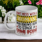 "Don't Mess With a Woman Who Knows How to Stage a Crime Scene" ceramic mug by Laser Design Creations, featuring caution tape and blood splatter details.
