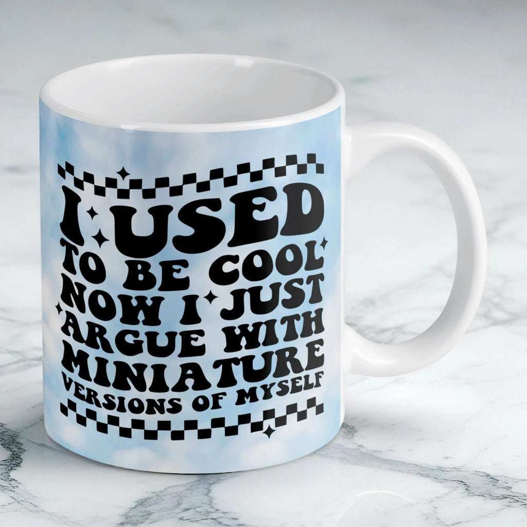 Reverse side of I Used To Be Cool mug, retro wavy text reading "I USED TO BE COOL NOW I JUST ARGUE WITH MINIATURE VERSIONS OF MYSELF" with blue clouds by Laser Design Creations.
