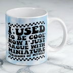 Reverse side of I Used To Be Cool mug, retro wavy text reading "I USED TO BE COOL NOW I JUST ARGUE WITH MINIATURE VERSIONS OF MYSELF" with blue clouds by Laser Design Creations.