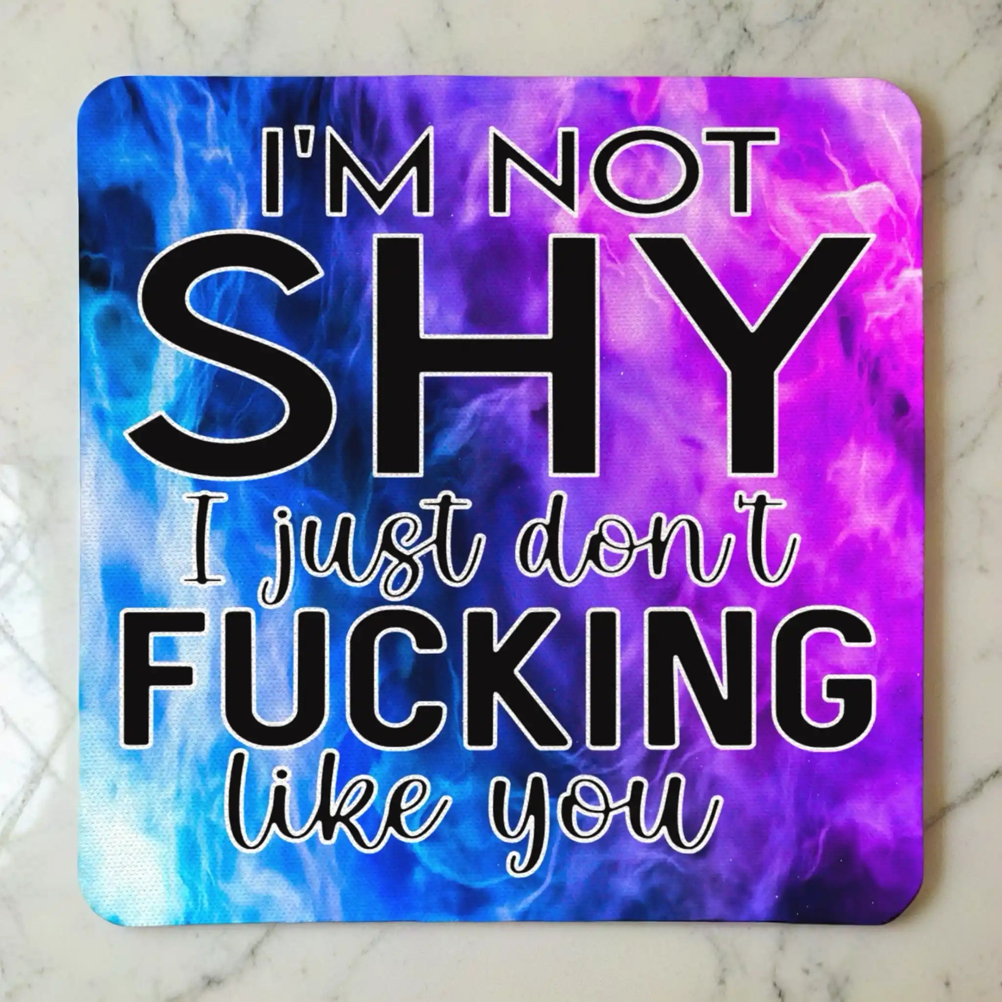 Top view of I'm Not Shy I Don't Like You neoprene coaster with the sarcastic text overlaying a vibrant purple watercolour nebula smoke design, by Laser Design Creations.