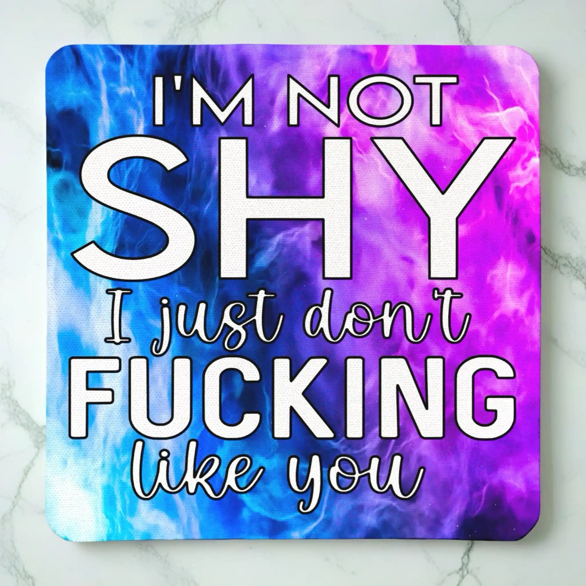 Top view of I'm Not Shy I Don't Like You neoprene coaster with the sarcastic text overlaying a vibrant purple watercolour nebula smoke design, by Laser Design Creations.