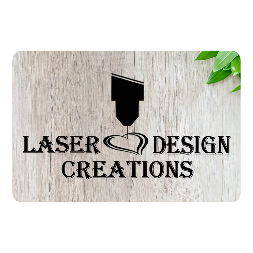 A rectangular sign with a light wood grain texture, featuring the black text 'LASER DESIGN CREATIONS' and a laser pointer graphic. The sign is shown on a white background with a small green leaf in the top right corner.