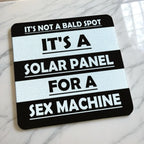Side view of Not A Bald Spot Solar Panel neoprene coaster with its non-slip black base on a tabletop, by Laser Design Creations.