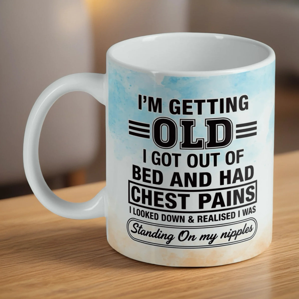 Standing On My Nipples ceramic mug by Laser Design Creations, featuring bold cheeky typography about getting older with a vibrant watercolour splash background.