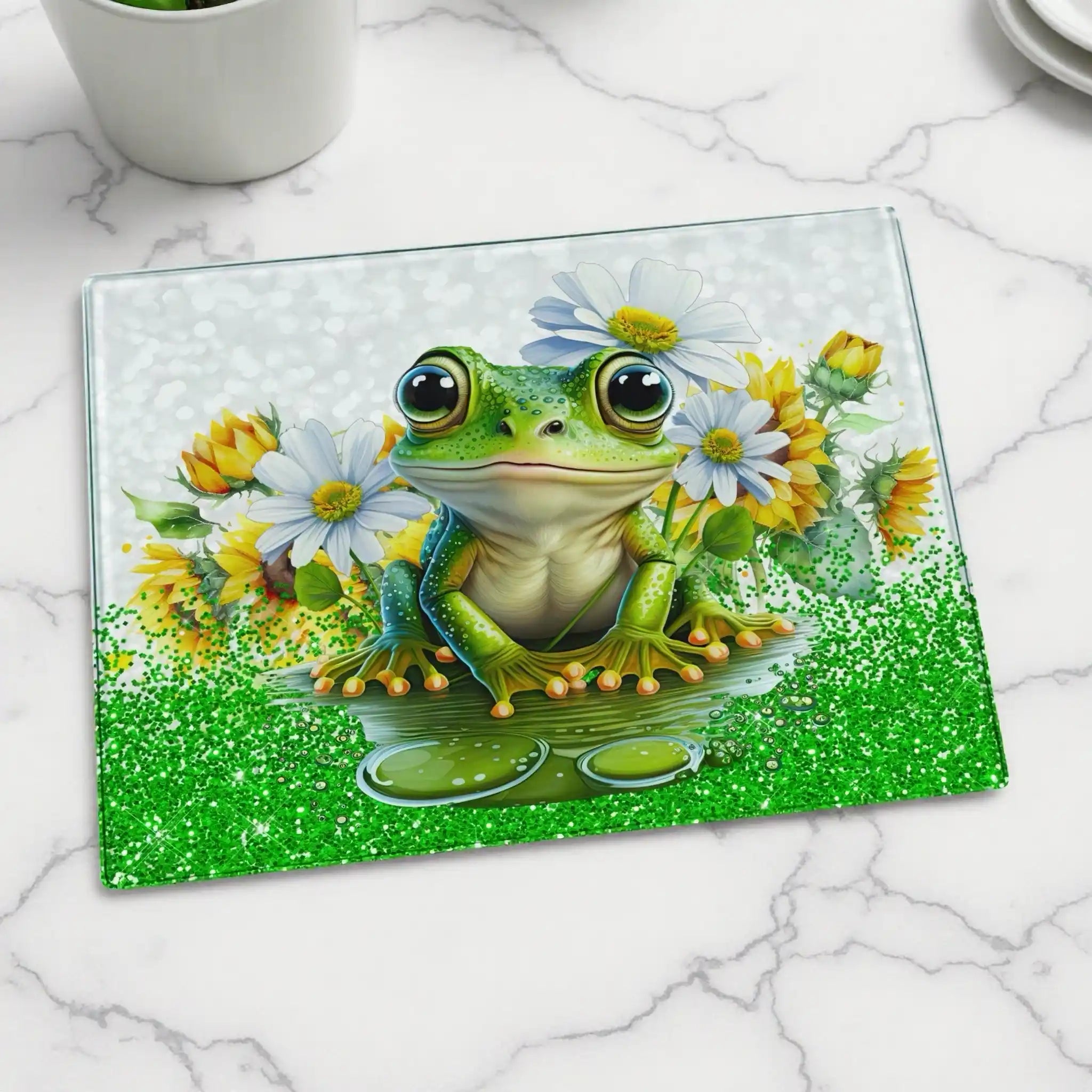Cute Frog Daisy Sunflower glass chopping board by Laser Design Creations, featuring a happy green frog surrounded by bright yellow sunflowers and white daisies. Displayed on a marble countertop.