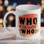 'Who Rescued Who' Quote ceramic mug, showcasing the heartfelt message in black typography over a soft peach watercolour splotch by Laser Design Creations.