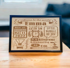 A personalized wooden plaque with engraved baby name birth details, displayed on a table.