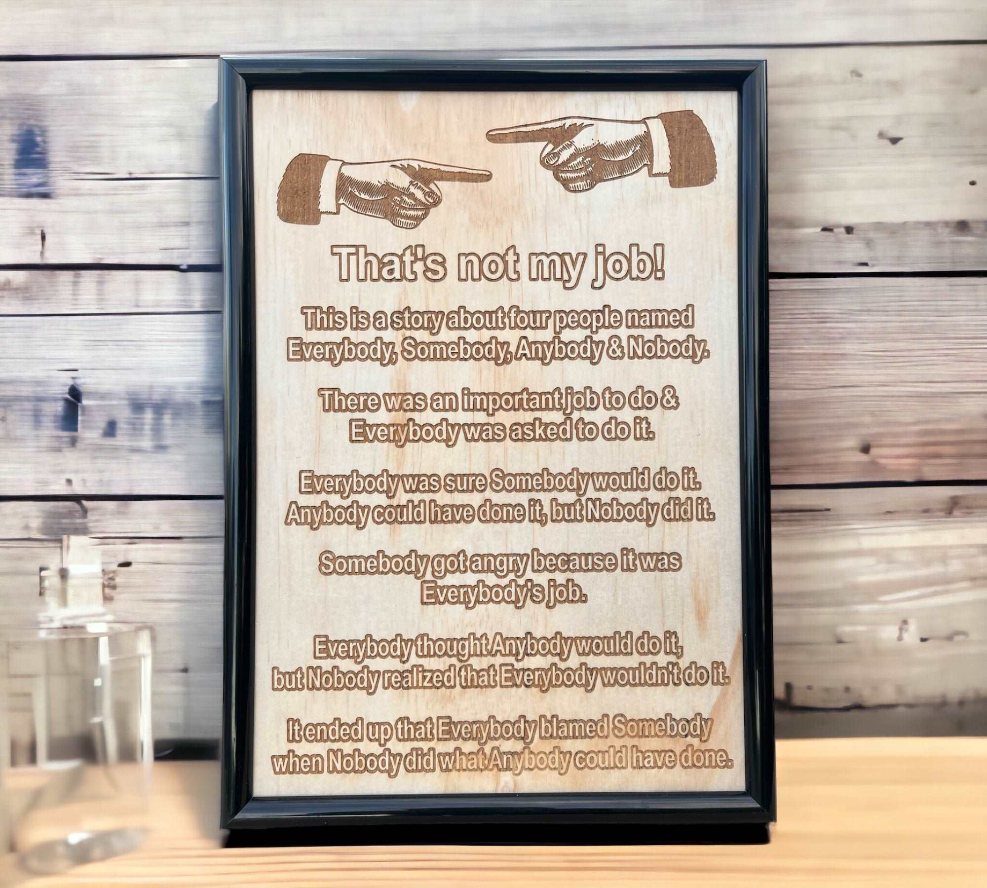 Wood engraved framed design with the phrase 'That's not my job!' humorous text, and a gun illustration. Displayed against a wooden background.