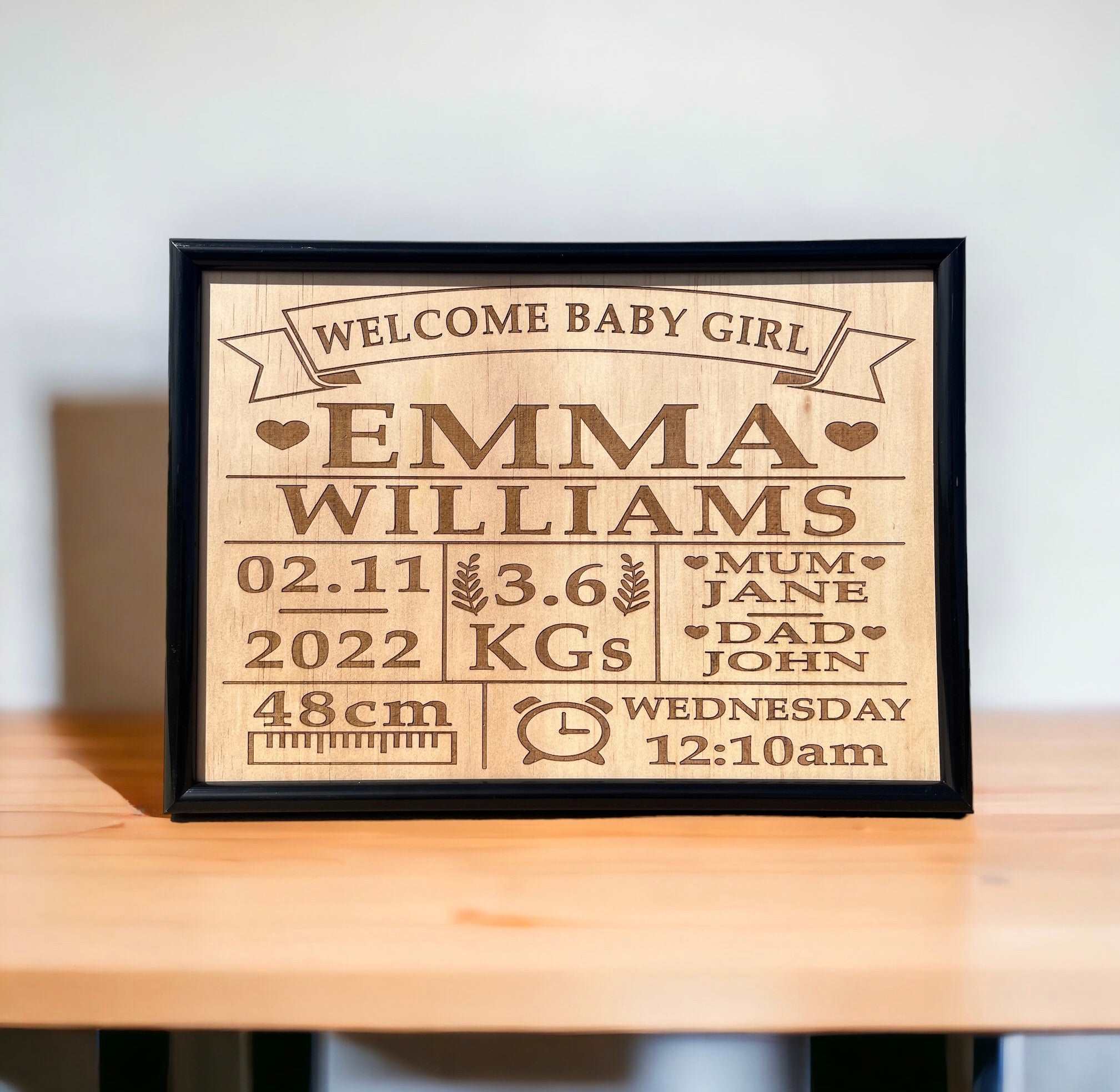 A personalized wooden plaque with engraved baby name birth details, displayed on a wooden table.
