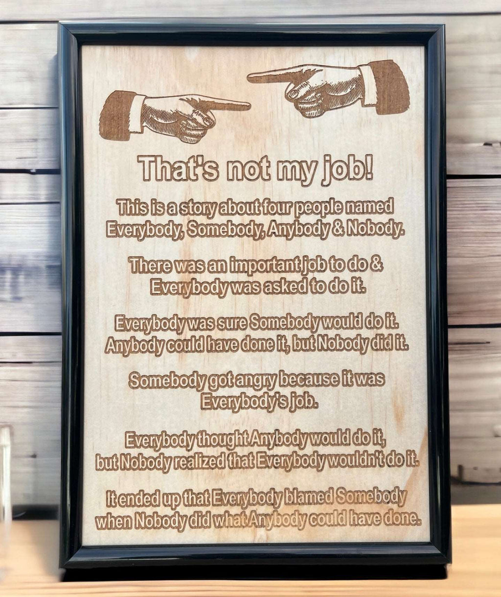 Wood engraved framed design with the phrase 'That's not my job!' humorous text, and a gun illustration. Displayed against a wooden background.