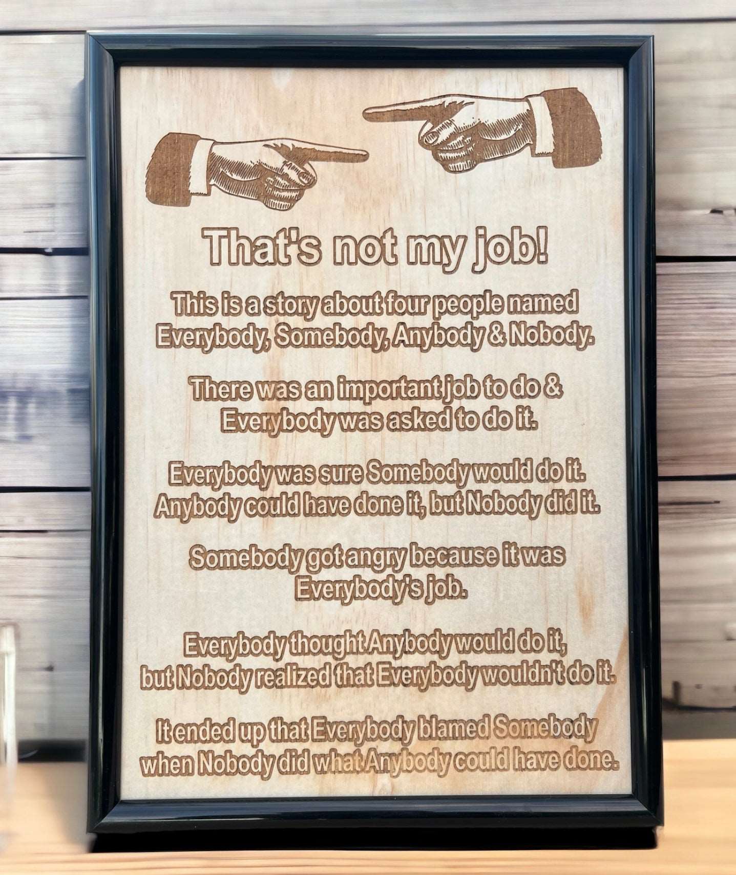Wood engraved framed design with the phrase 'That's not my job!' humorous text, and a gun illustration. Displayed against a wooden background.