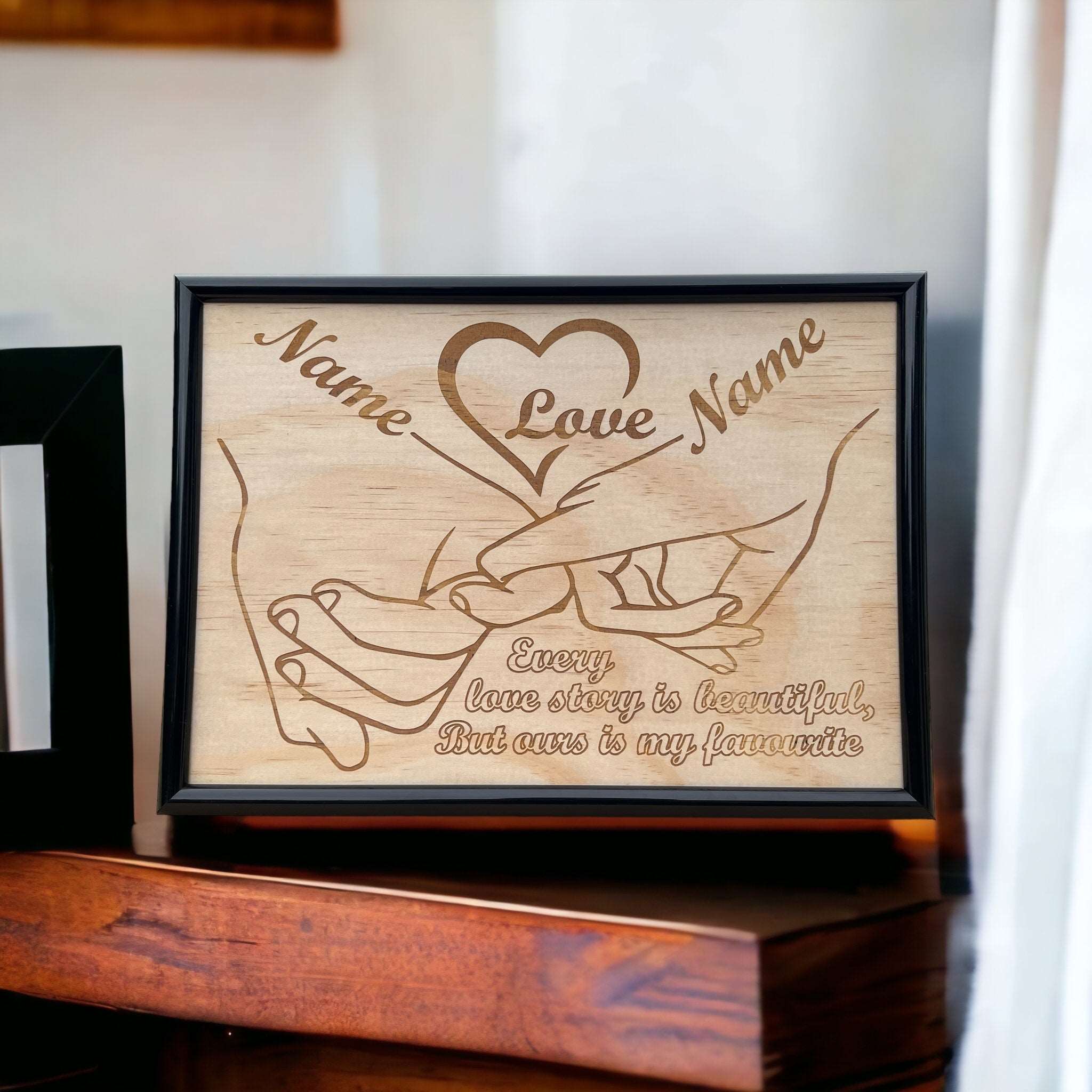 A wood engraved framed design with the phrase 'Every love story is beautiful, But ours is my favourite' and two placeholder names. The design features intertwined hands and a heart shape.