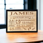 A personalized wooden plaque with engraved baby name birth details, displayed on a wooden bench.